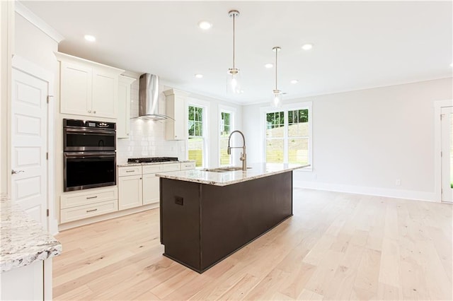 kitchen featuring double wall oven, a sink, light wood-style floors, wall chimney range hood, and decorative backsplash