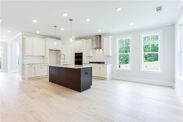 kitchen with wall chimney range hood, ornamental molding, white cabinets, gas stovetop, and a sink