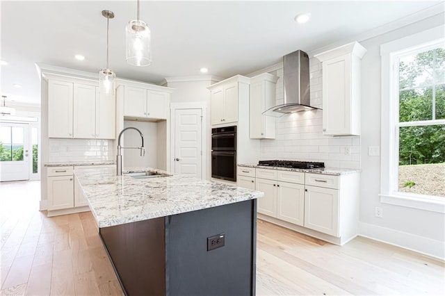 kitchen with dobule oven black, a sink, gas stovetop, white cabinets, and wall chimney exhaust hood