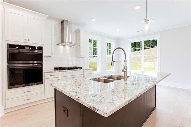 kitchen featuring gas cooktop, stainless steel double oven, a sink, wall chimney range hood, and backsplash