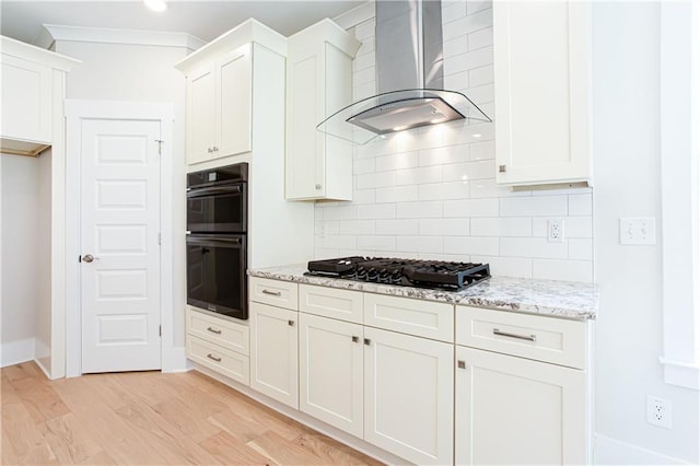 kitchen featuring backsplash, light stone counters, light wood-style flooring, black appliances, and wall chimney exhaust hood