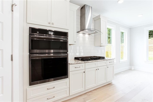 kitchen with black gas cooktop, white cabinets, light stone countertops, stainless steel double oven, and wall chimney exhaust hood