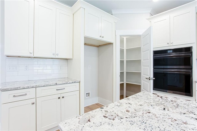 kitchen featuring tasteful backsplash, white cabinets, light stone countertops, and stainless steel double oven