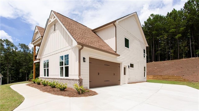 view of side of home with brick siding, board and batten siding, concrete driveway, roof with shingles, and an attached garage