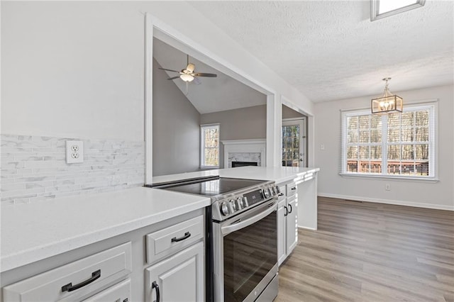 kitchen featuring lofted ceiling, a textured ceiling, white cabinets, ceiling fan with notable chandelier, and stainless steel range with electric cooktop