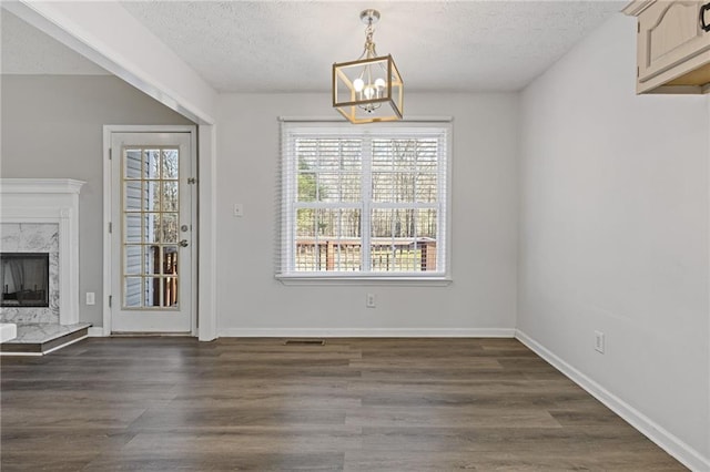 unfurnished dining area with an inviting chandelier, a high end fireplace, dark hardwood / wood-style flooring, and a textured ceiling