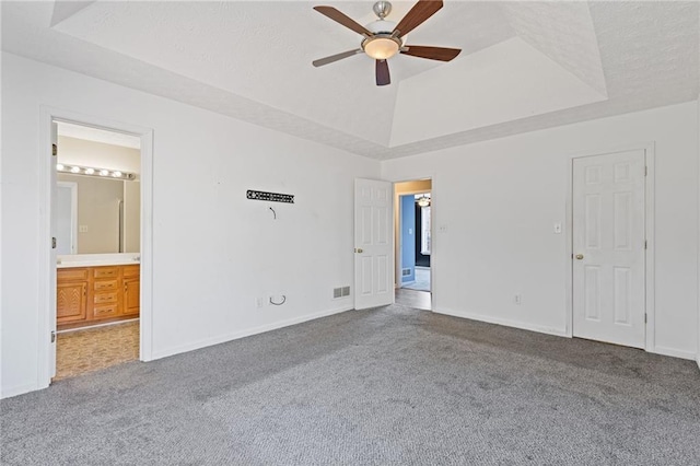 unfurnished bedroom with connected bathroom, a tray ceiling, ceiling fan, and carpet flooring