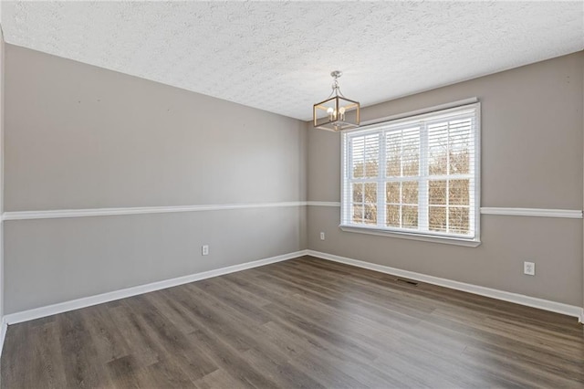 empty room with an inviting chandelier, dark hardwood / wood-style floors, and a textured ceiling