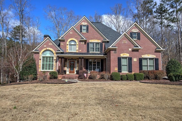 view of front of home with covered porch, brick siding, a chimney, and a front lawn