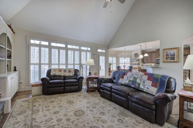 living area featuring light wood-type flooring, high vaulted ceiling, arched walkways, and a ceiling fan