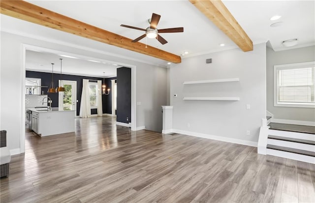 unfurnished living room with wood-type flooring, beam ceiling, ceiling fan with notable chandelier, sink, and crown molding