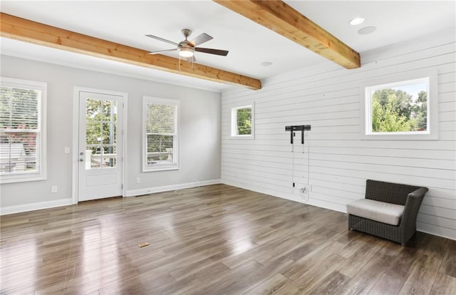 unfurnished room featuring ceiling fan, dark hardwood / wood-style floors, beamed ceiling, and a healthy amount of sunlight