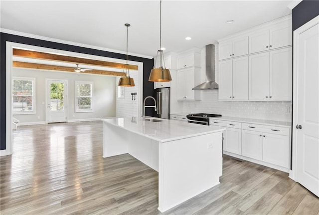 kitchen with decorative light fixtures, beamed ceiling, light hardwood / wood-style flooring, a kitchen island with sink, and wall chimney exhaust hood