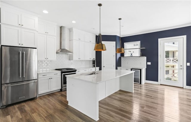 kitchen featuring appliances with stainless steel finishes, pendant lighting, wall chimney range hood, a center island with sink, and dark hardwood / wood-style floors