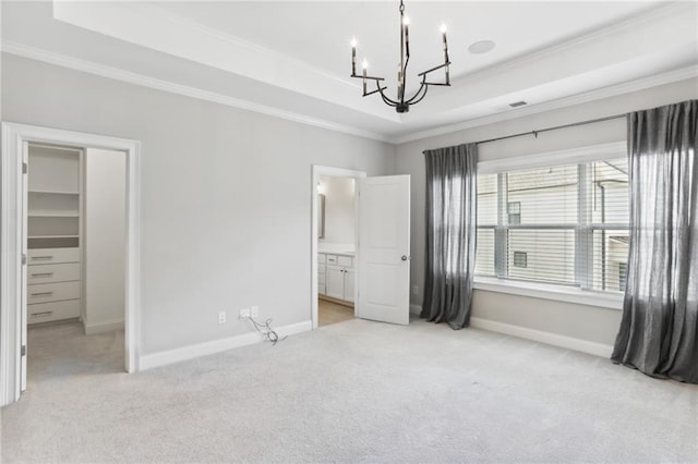 unfurnished bedroom featuring a walk in closet, a tray ceiling, light carpet, ensuite bath, and a notable chandelier