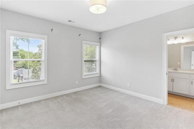 unfurnished bedroom featuring connected bathroom, light colored carpet, and multiple windows