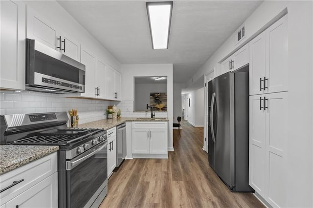 kitchen featuring light stone countertops, appliances with stainless steel finishes, backsplash, sink, and white cabinets