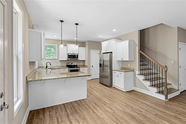 kitchen with appliances with stainless steel finishes, a peninsula, light wood-style floors, light stone countertops, and white cabinetry