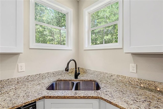 kitchen view of a sink, white cabinets, and light stone counters