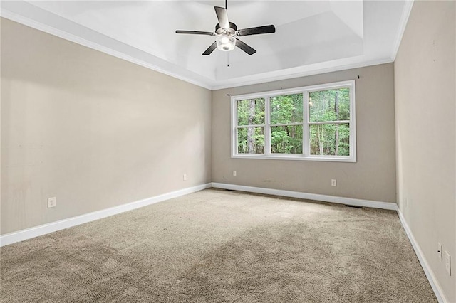 carpeted spare room with a raised ceiling, ceiling fan, baseboards, and ornamental molding