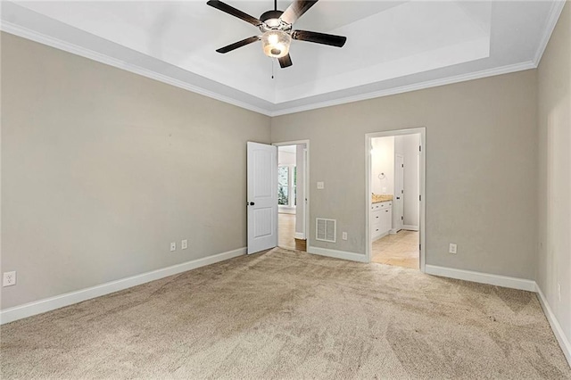 unfurnished bedroom with light carpet, baseboards, ornamental molding, a tray ceiling, and ensuite bathroom