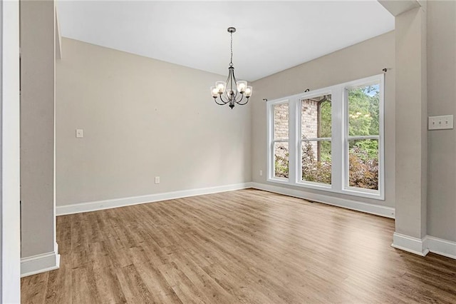 empty room featuring baseboards, wood finished floors, and a chandelier