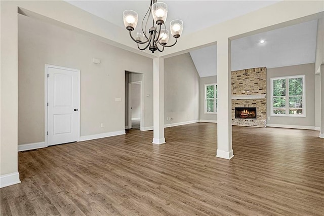 unfurnished living room with healthy amount of natural light, a chandelier, wood finished floors, and vaulted ceiling