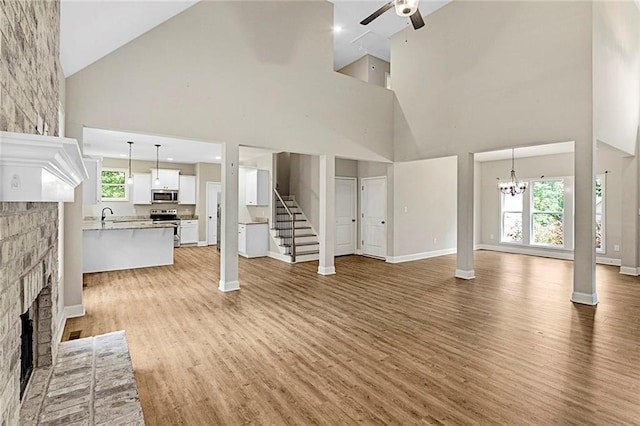 unfurnished living room with high vaulted ceiling, a ceiling fan, a fireplace, stairs, and light wood-style flooring