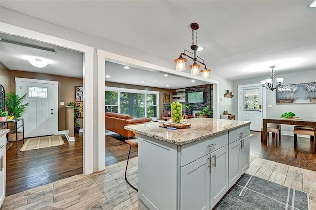 kitchen featuring pendant lighting, a center island, a kitchen breakfast bar, light stone countertops, and a chandelier