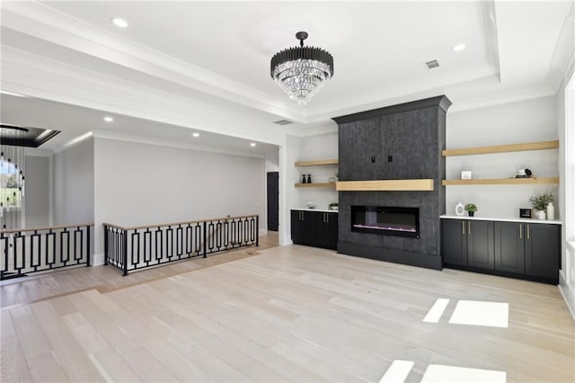 unfurnished living room with a chandelier, light wood-style floors, recessed lighting, crown molding, and a tray ceiling