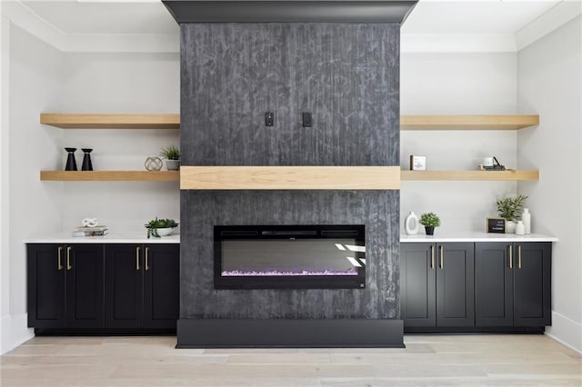 bar area featuring light wood finished floors, a glass covered fireplace, and ornamental molding