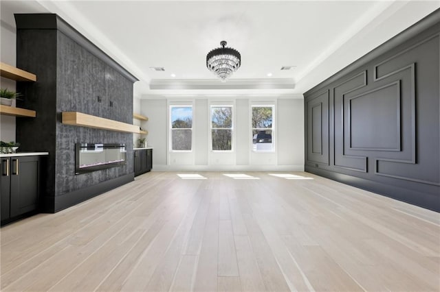 unfurnished living room with a raised ceiling, light wood-type flooring, a large fireplace, a chandelier, and recessed lighting