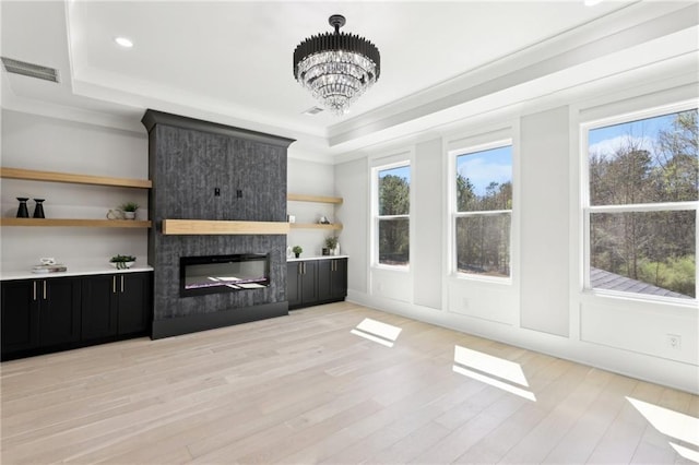 unfurnished living room with a raised ceiling, plenty of natural light, ornamental molding, light wood-type flooring, and a chandelier
