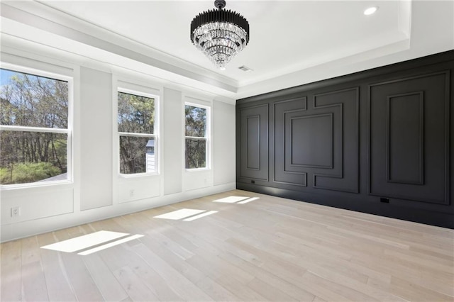 unfurnished bedroom featuring a decorative wall, a chandelier, a tray ceiling, and wood finished floors