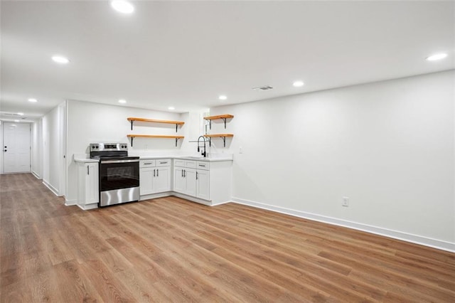 kitchen featuring open shelves, a sink, light countertops, light wood finished floors, and stainless steel electric range