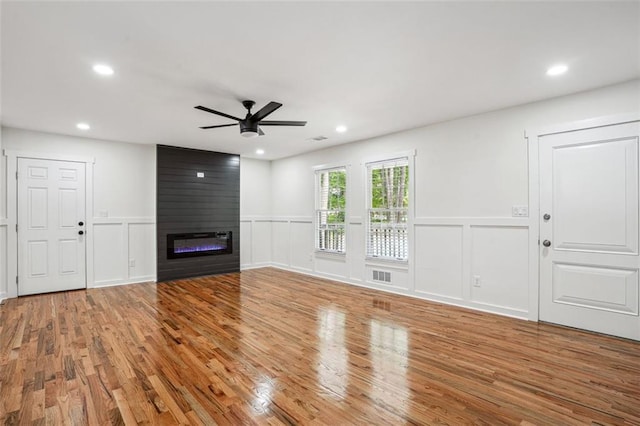 unfurnished living room with a fireplace, wood finished floors, ceiling fan, and a decorative wall