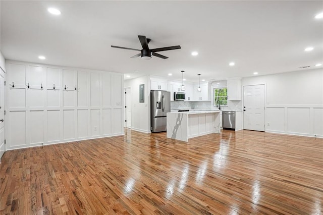 unfurnished living room with a sink, ceiling fan, recessed lighting, light wood finished floors, and a decorative wall
