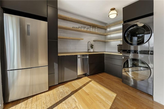 kitchen featuring stacked washer and dryer, stainless steel appliances, sink, and light hardwood / wood-style flooring