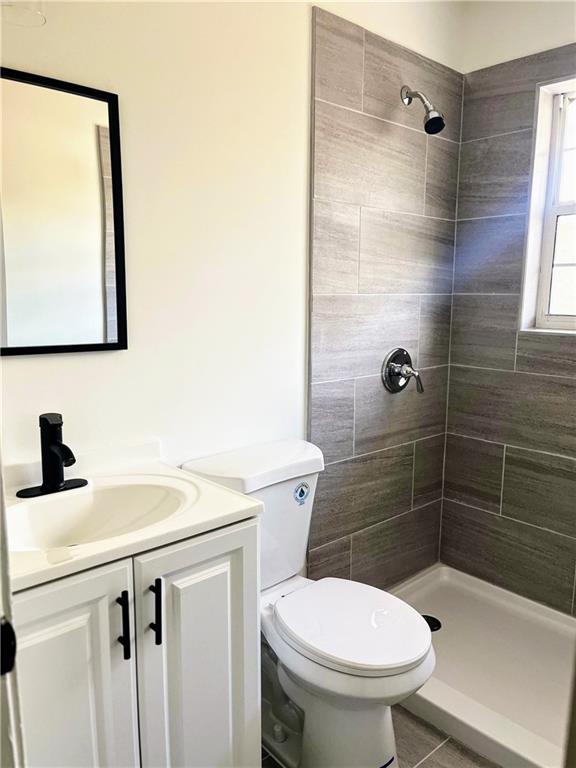 bathroom with vanity, a tile shower, tile patterned floors, and toilet