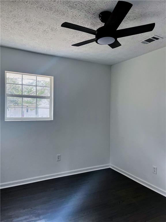 empty room with ceiling fan, dark hardwood / wood-style flooring, and a textured ceiling