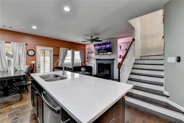 kitchen featuring dark wood-type flooring, a sink, a kitchen island with sink, light countertops, and stainless steel dishwasher