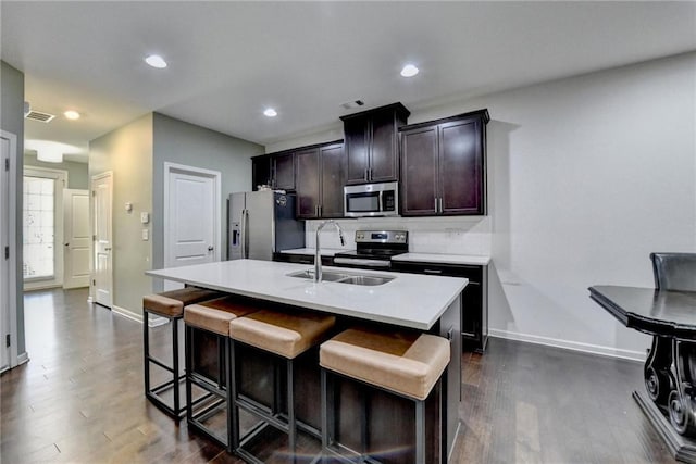 kitchen featuring a kitchen island with sink, a breakfast bar, a sink, light countertops, and appliances with stainless steel finishes