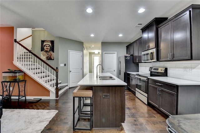 kitchen with stainless steel appliances, a sink, light countertops, an island with sink, and a kitchen bar