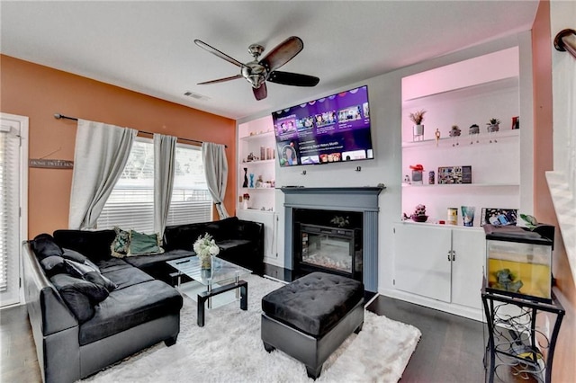 living area featuring a glass covered fireplace, visible vents, ceiling fan, and wood finished floors