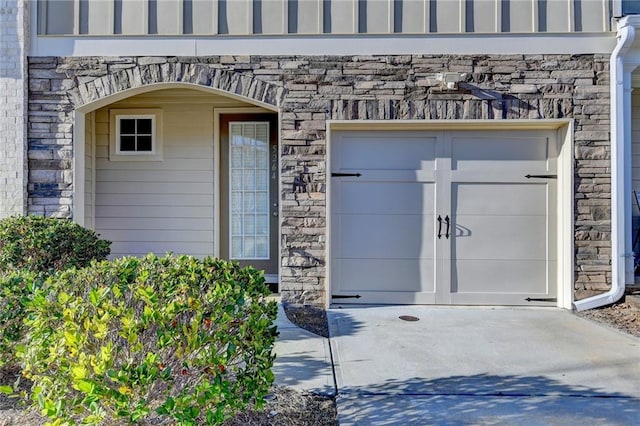 view of exterior entry featuring a garage, stone siding, driveway, and board and batten siding