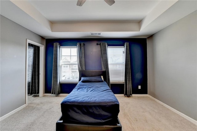 carpeted bedroom with a tray ceiling, a ceiling fan, visible vents, and baseboards