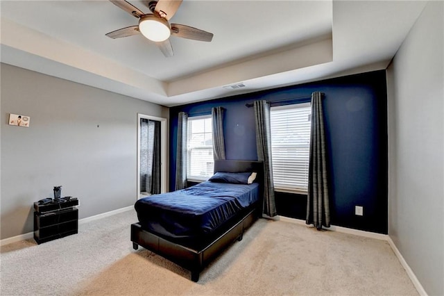 bedroom featuring a raised ceiling, light colored carpet, and baseboards