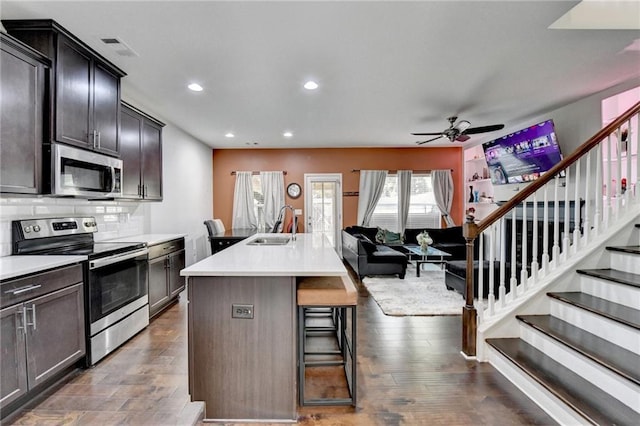 kitchen featuring an island with sink, appliances with stainless steel finishes, a kitchen breakfast bar, open floor plan, and light countertops