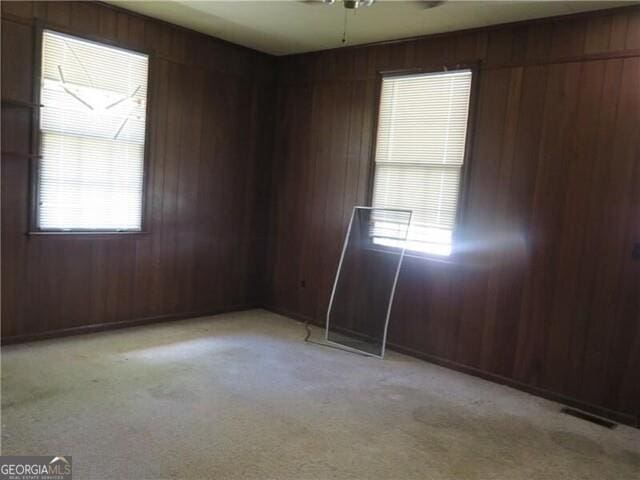 spare room with light colored carpet, ceiling fan, and wood walls