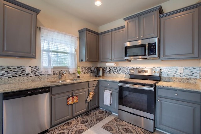 kitchen with gray cabinetry, sink, light stone counters, and appliances with stainless steel finishes